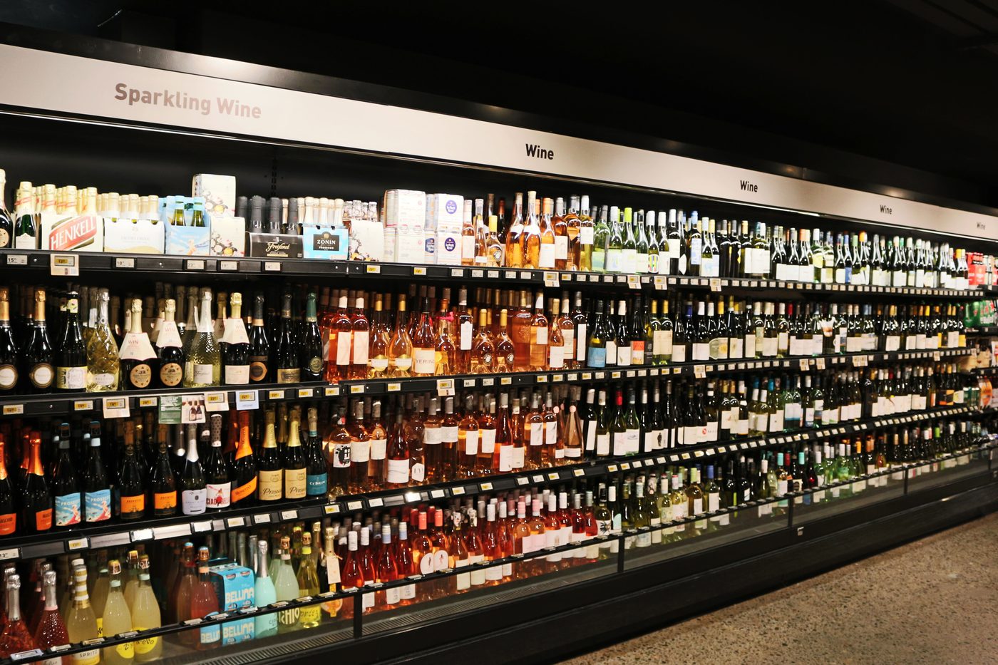 A run of open wine cabinets seen head on, sparkling wine to the left and still wine along the rest, with a black blade on every shelf edge