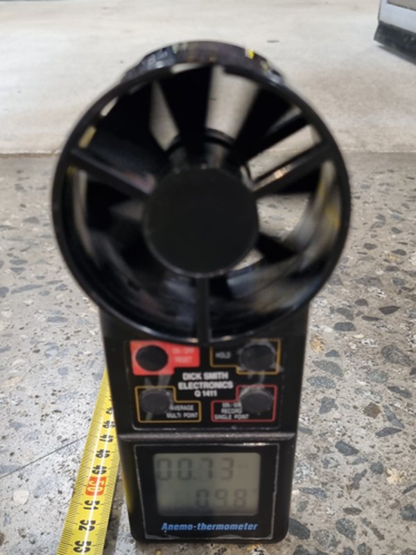 An anemometer display reading 0.73 metres a second and 9.8 degrees, beside a measuring tape