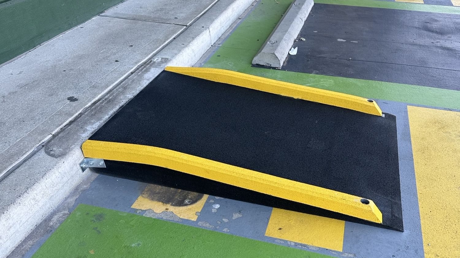 Kerb ramp with yellow edges bolted between a pickup bay and the footpath