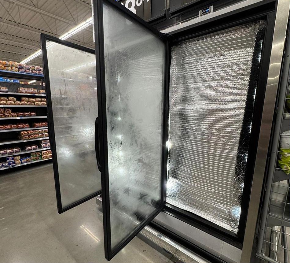 An open freezer door in a supermarket aisle with the untreated glass gone completely white with condensation, hiding the product behind it