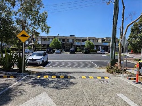 A speed hump sign beside humps at a car park entry